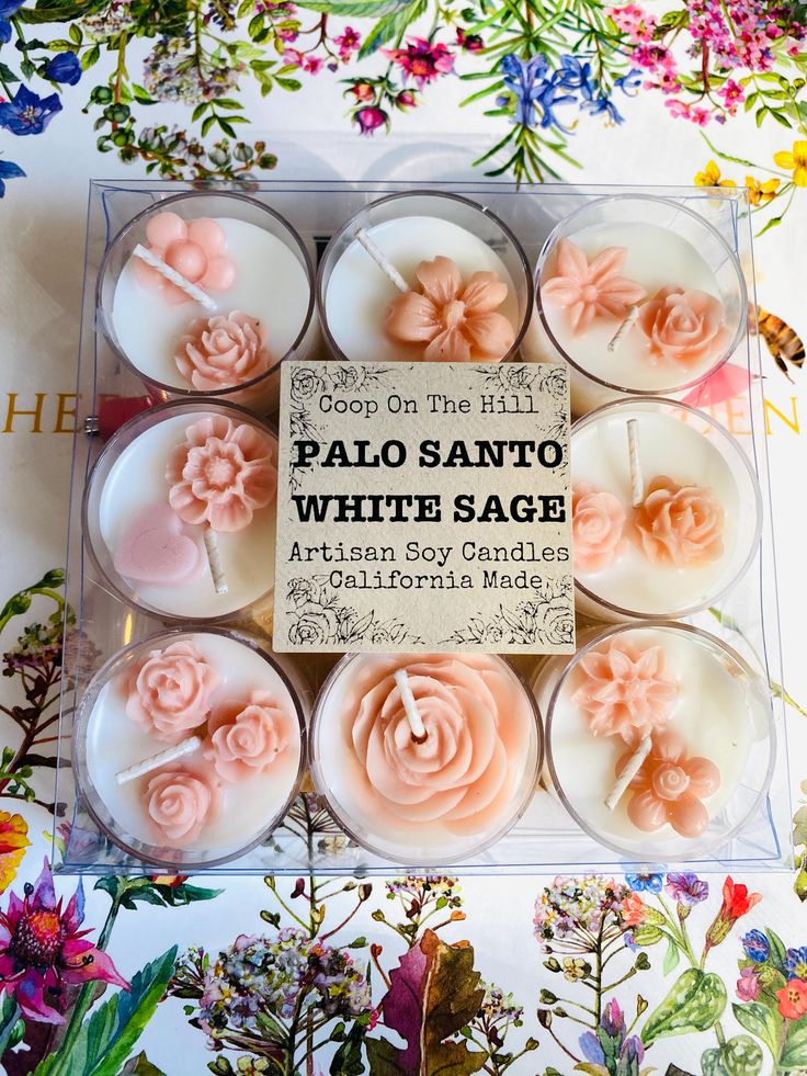 six candles with pink flowers in the middle and white frosting on top, surrounded by wildflowers