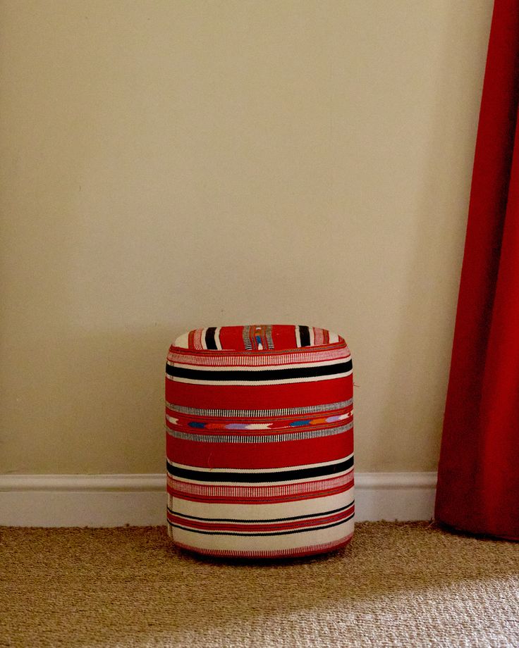 a red and black striped basket sitting on the floor next to a curtained window