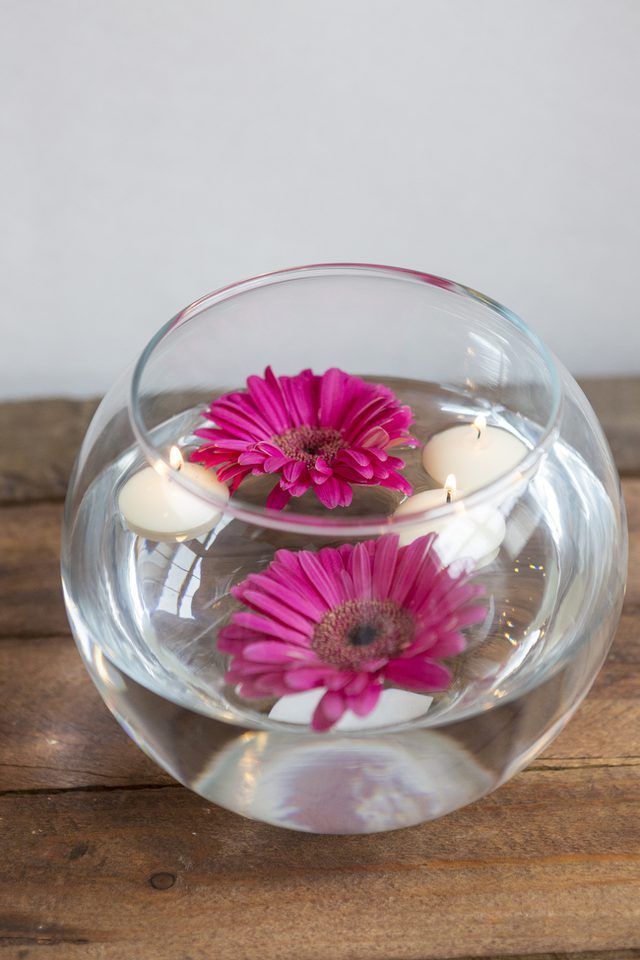 two pink flowers floating in a clear bowl with candles on the side and water inside