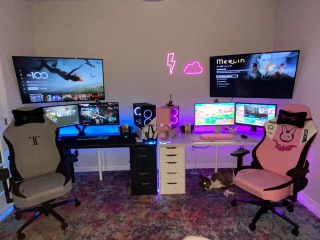 a room with three computer monitors and two gaming screens on the wall, all in different colors