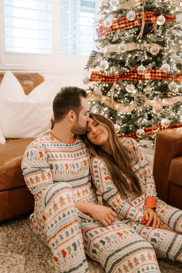 a man and woman in pajamas sitting next to a christmas tree