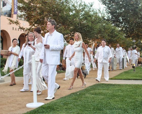 a group of people dressed in white walking down a sidewalk