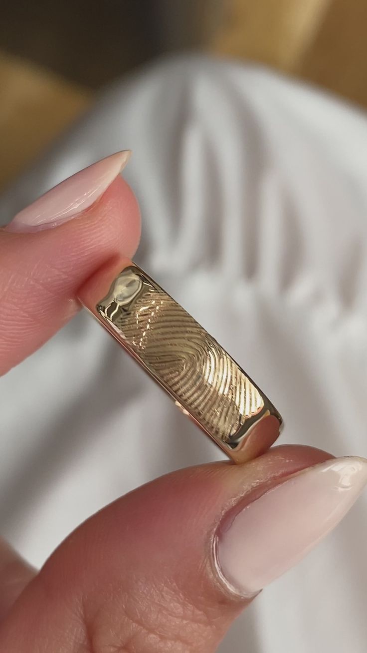 a close up of a person's hand holding a gold ring with finger prints on it