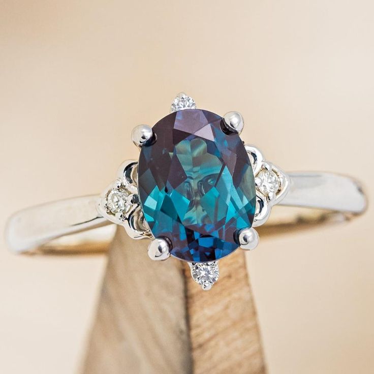 a ring with a blue topaz surrounded by white diamonds on a wooden stand in front of a beige background