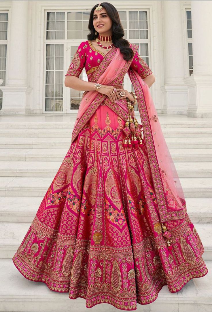 a woman in a pink and gold lehenga standing on steps with her hand on her hip