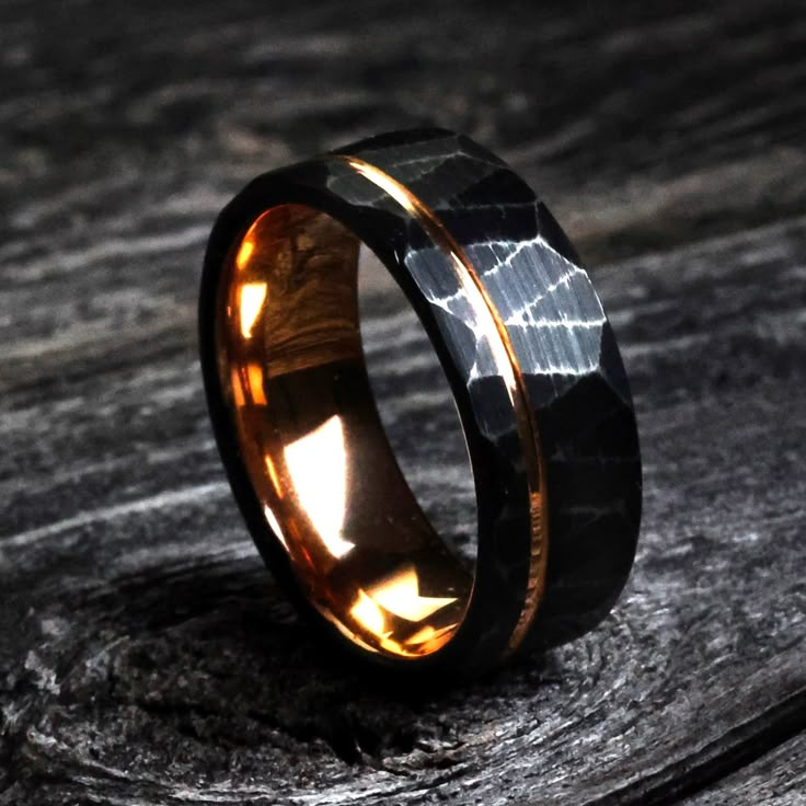 a black and gold wedding ring on top of a piece of wood with the light shining through