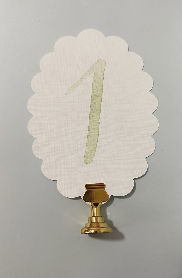 the number one is painted on top of a white piece of paper with a gold base