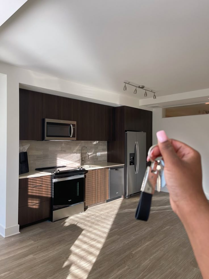 a person holding up a remote control to take a picture of a kitchen in the background