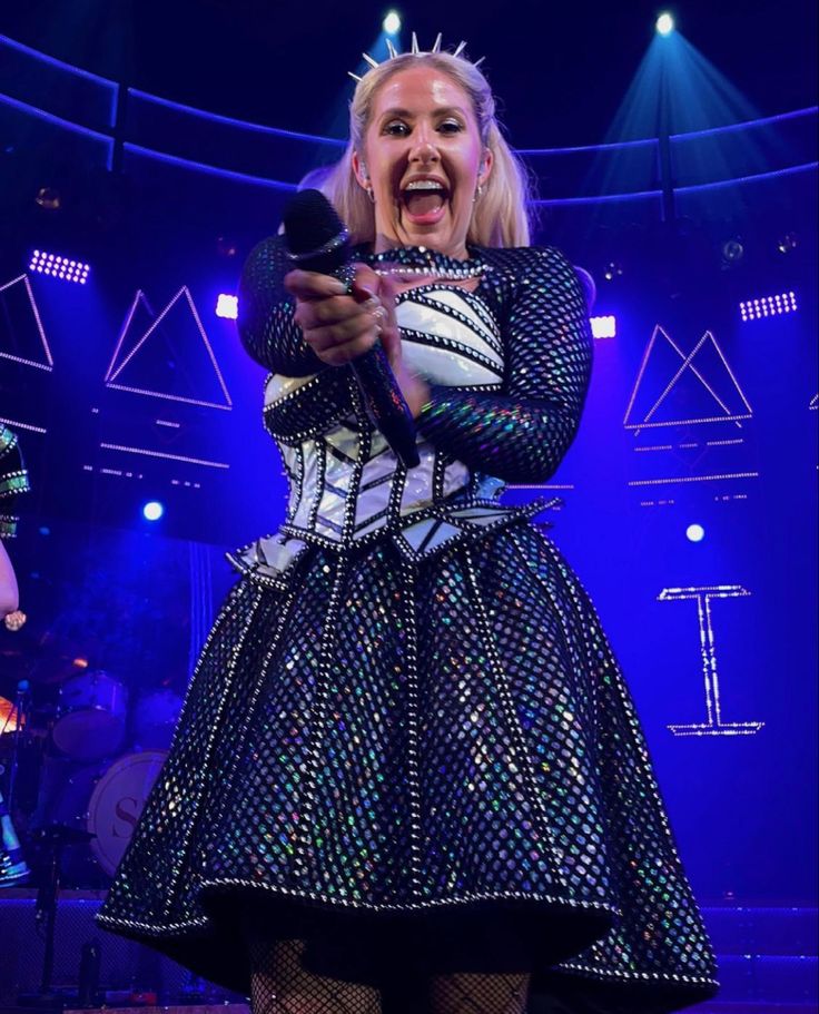 a woman in a black and white dress holding a cell phone while standing on stage