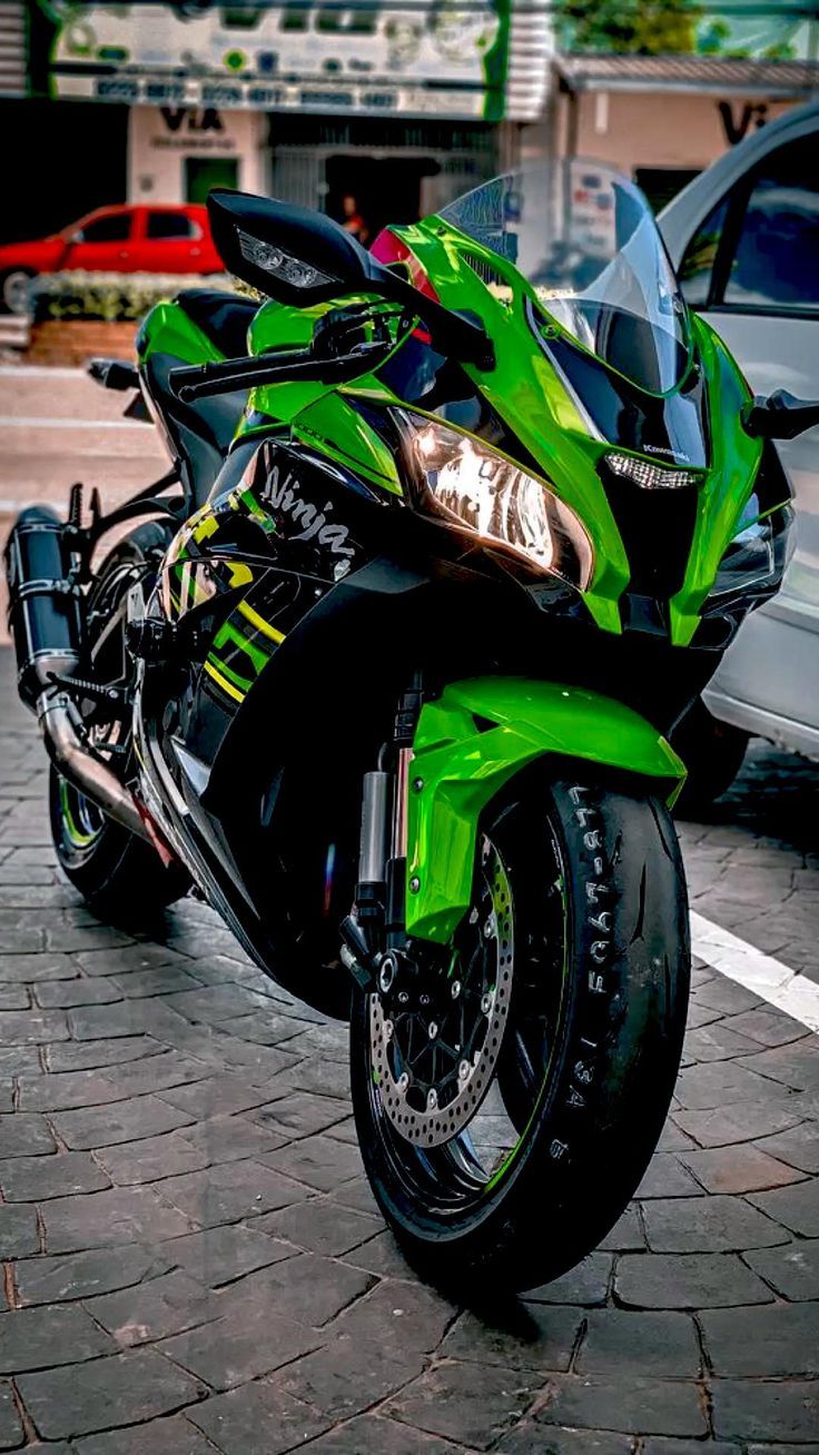 a green motorcycle parked next to a silver car