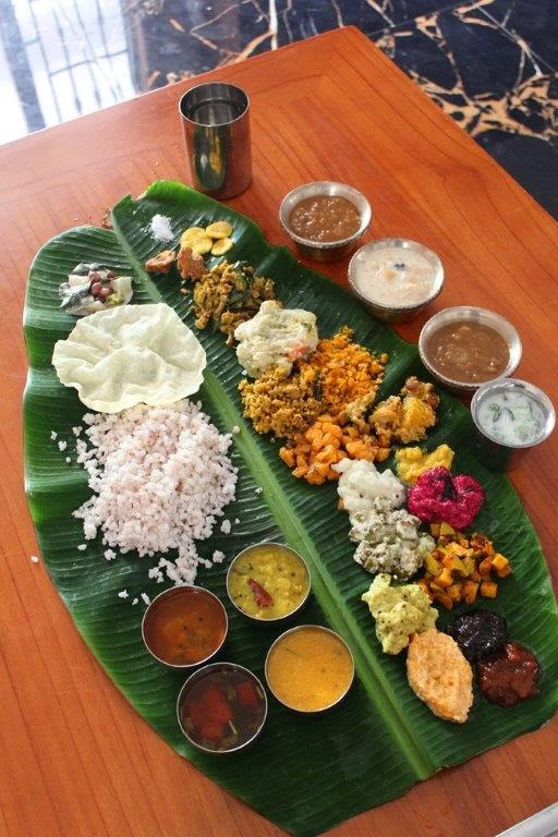 a banana leaf filled with different types of food on top of a wooden table next to cups and sauces