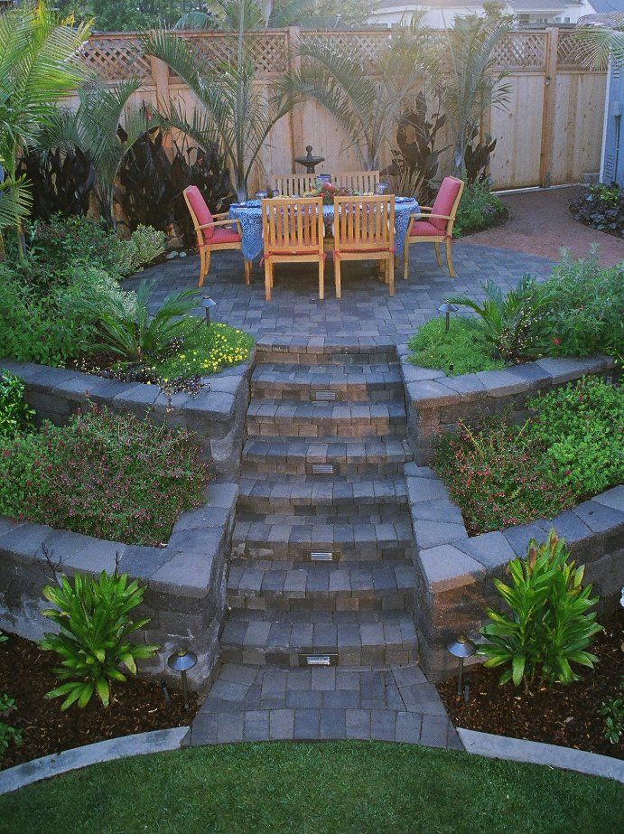 a patio with steps leading up to a table and chairs in the middle of it