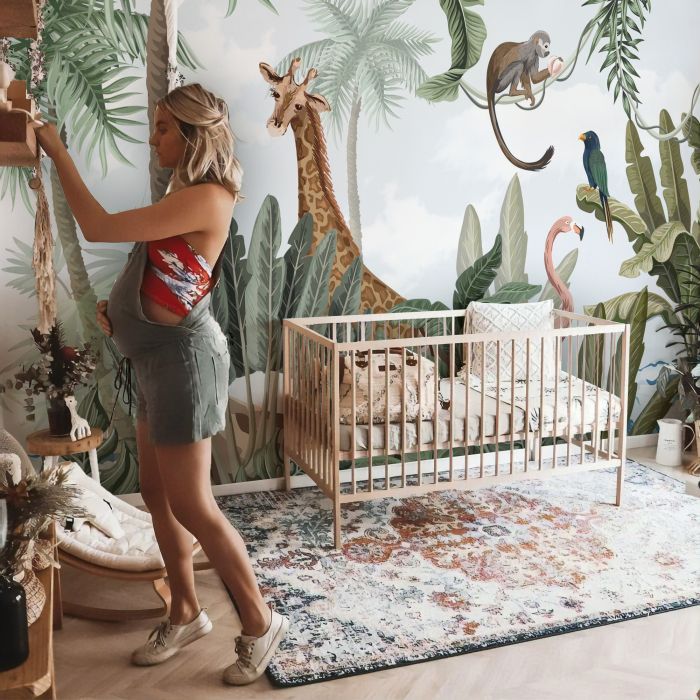 a woman standing next to a baby crib in front of a jungle wall mural