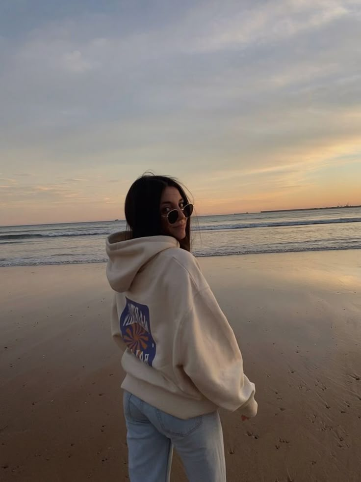 a woman standing on top of a sandy beach next to the ocean at sun set