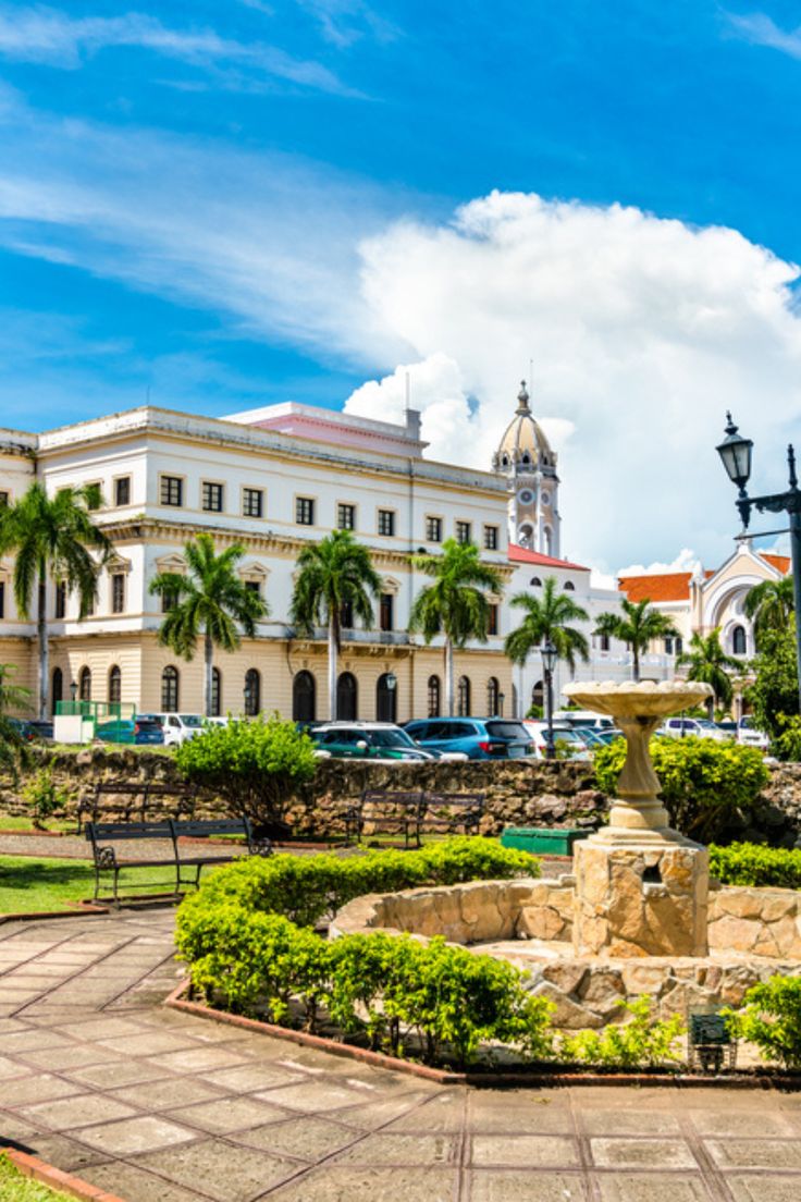 a large white building sitting next to a lush green park filled with trees and bushes