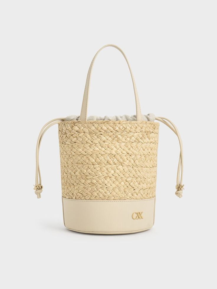 The quintessential bucket bag with a summer-friendly twist. This piece features a classic cylindrical shape, with a leather bottom offering a smooth contrast to the intricate woven finish and providing extra stability. It also includes a drawstring closure for quick and easy access to your belongings while keeping them safe and secure. The emblem adds a subtle touch of glamour in gold, further elevating this sophisticated design. Cheap Summer Cream Bucket Bag, Cheap Gold Bucket Bag, Beige Woven Leather Bucket Bag, Natural Woven Leather Bucket Bag, Luxury Leather Basket Bucket Bag, Luxury Leather Bucket Bag For Spring, Modern Bucket Bag For Vacation, Luxury Spring Leather Bucket Bag, Chic Natural Leather Bucket Bag