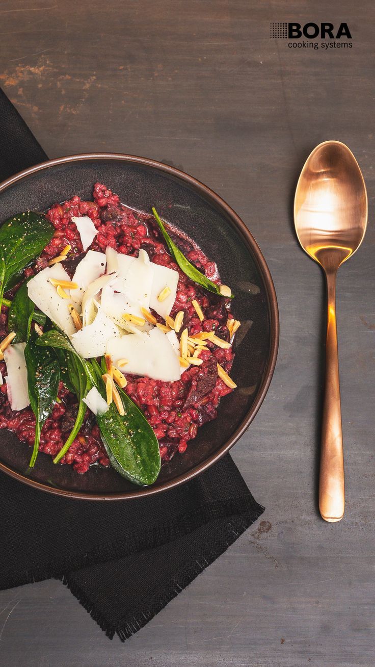 a black plate topped with meat and veggies next to a gold serving spoon