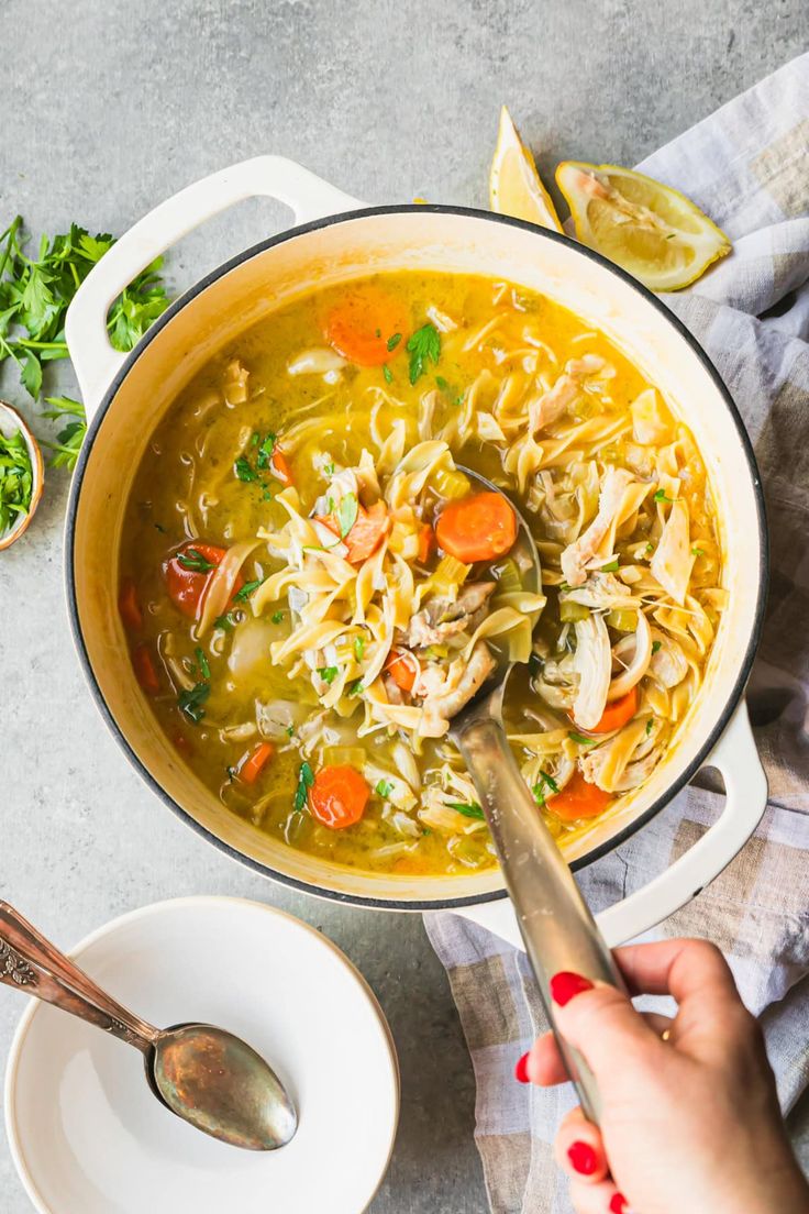 a person holding a spoon over a bowl of chicken noodle soup