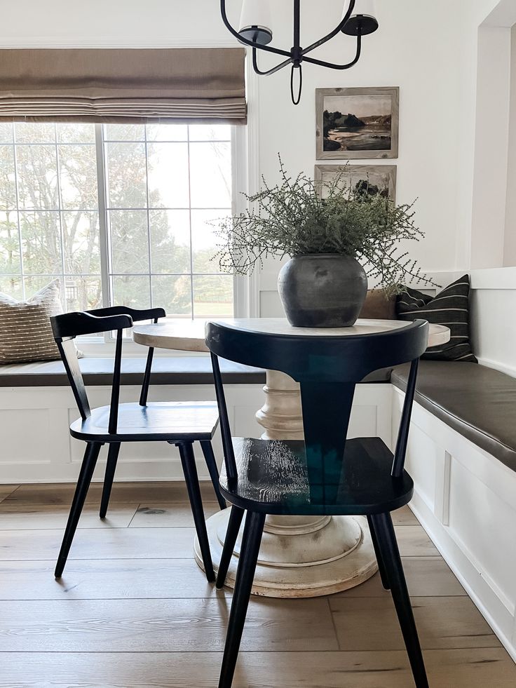 a dining room table with two chairs and a vase on top of it in front of a window