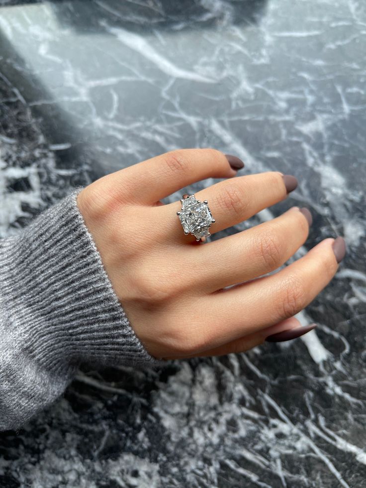 a woman's hand with a diamond ring on top of her finger, sitting on a marble surface