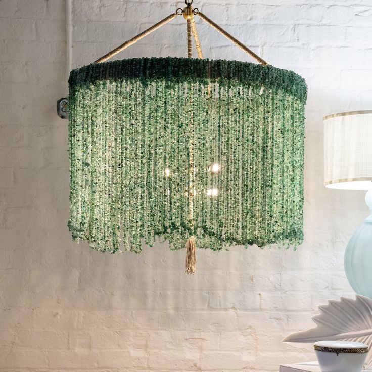 a green chandelier hanging from the ceiling next to a white vase and lamp