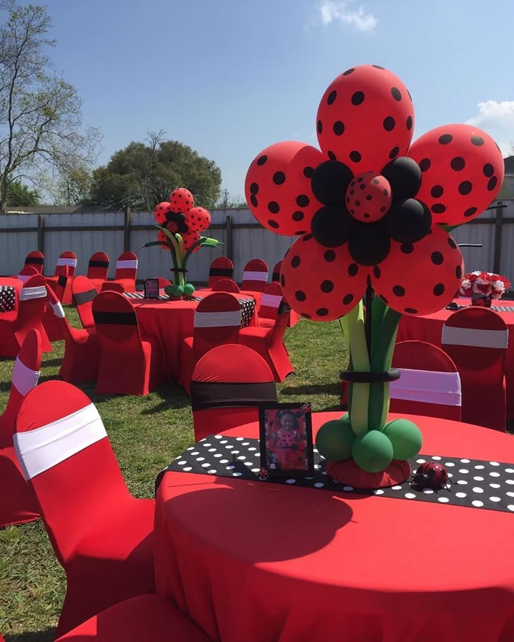 a red table topped with lots of ladybug balloons and place settings on top of it