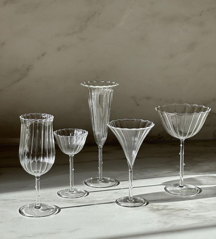 five wine glasses are lined up in a row on the floor, one is empty