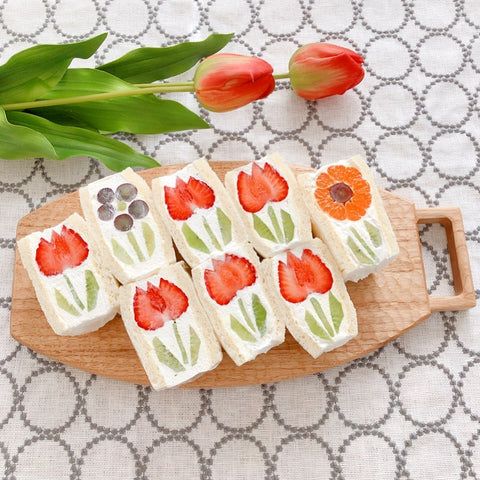 small pieces of food on a wooden tray next to tulips and an orange flower