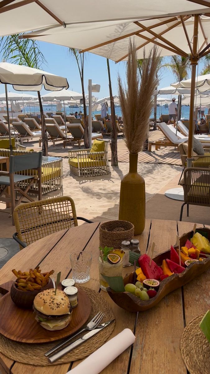 a wooden table topped with plates of food next to an umbrella covered beach side area