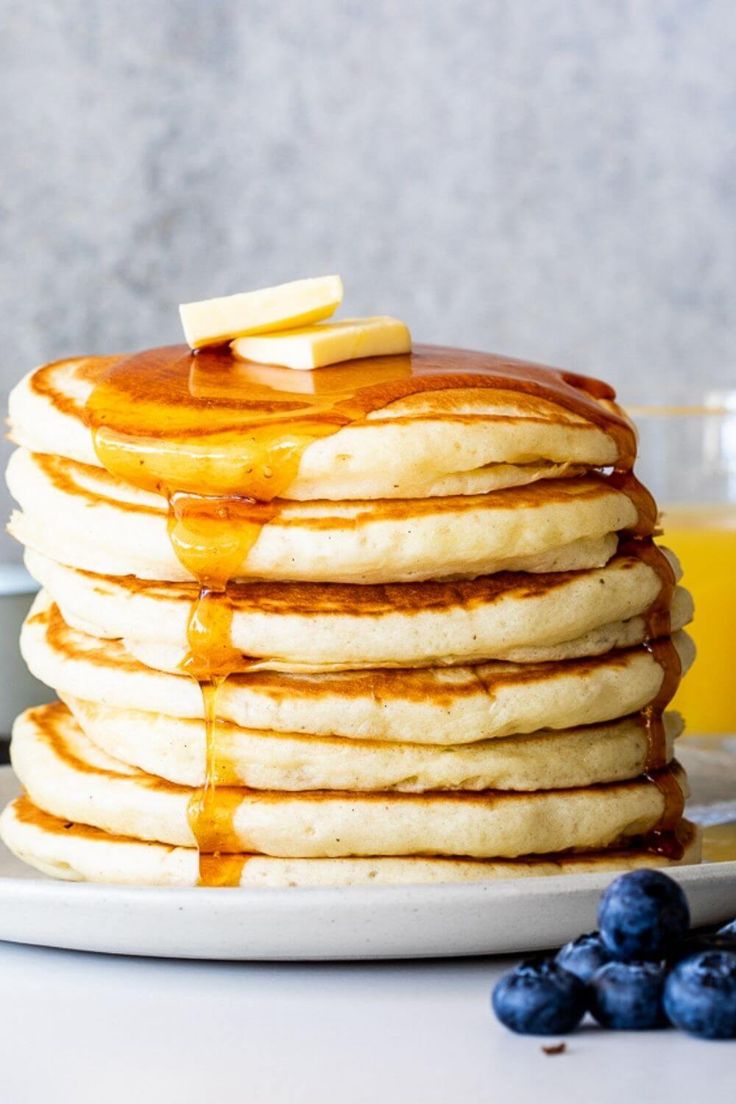 stack of pancakes with syrup and blueberries on the side next to a glass of orange juice