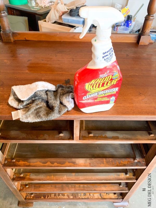 a cat laying on top of a wooden table next to a bottle of cleaning agent