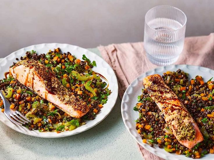 two white plates topped with fish and vegetables on top of a table next to a glass of water