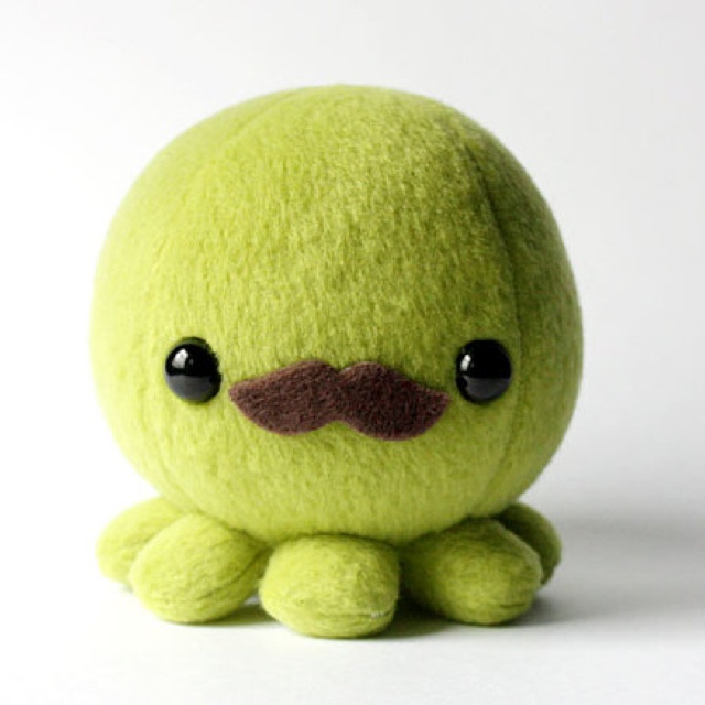 a green stuffed animal with a mustache on it's face, sitting in front of a white background