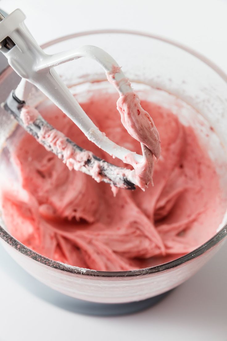 a mixer filled with pink colored food on top of a white counter