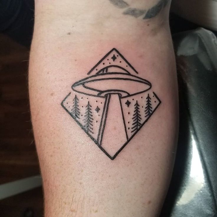 a black and white tattoo on the leg of a man with trees, mountains and an alien spaceship