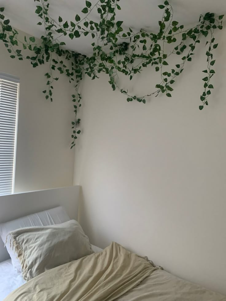 an unmade bed with white sheets and green vines hanging from the ceiling above it