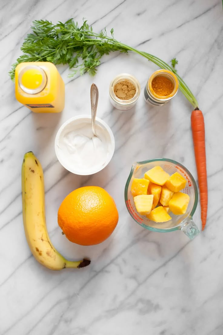 fruits and vegetables are arranged on a marble counter top, including bananas, oranges, yogurt, and other ingredients