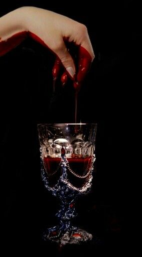 a person pouring red liquid into a wine goblet in the middle of a dark room