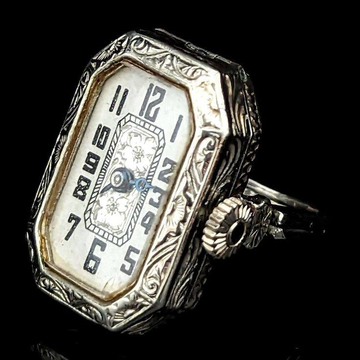 Presenting a remarkable Art Deco era ring watch convertible to wrist watch, a true novelty piece that encapsulates the elegance and ingenuity of the past. Crafted in 14k white gold, this antique/vintage piece features a double shank that cleverly opens up into watch lugs, allowing for the watch to be converted into a wrist watch with the addition of a cord strap (not included). The white dial adorned with Arabic numerals and beautiful floral accents sits within an exquisitely engraved case, a te Luxury Art Deco Watch With Manual Winding, Antique Platinum Jewelry And Watches For Gifts, Antique Platinum Jewelry And Watches As Gifts, Vintage Formal Watches With Rotating Bezel, Antique Platinum Watches For Anniversary, Antique Watch Accessories With Polished Finish, Antique Platinum Jewelry And Watches For Evening, Vintage Wedding Jewelry And Watches With Polished Finish, Antique Platinum Watch For Gift