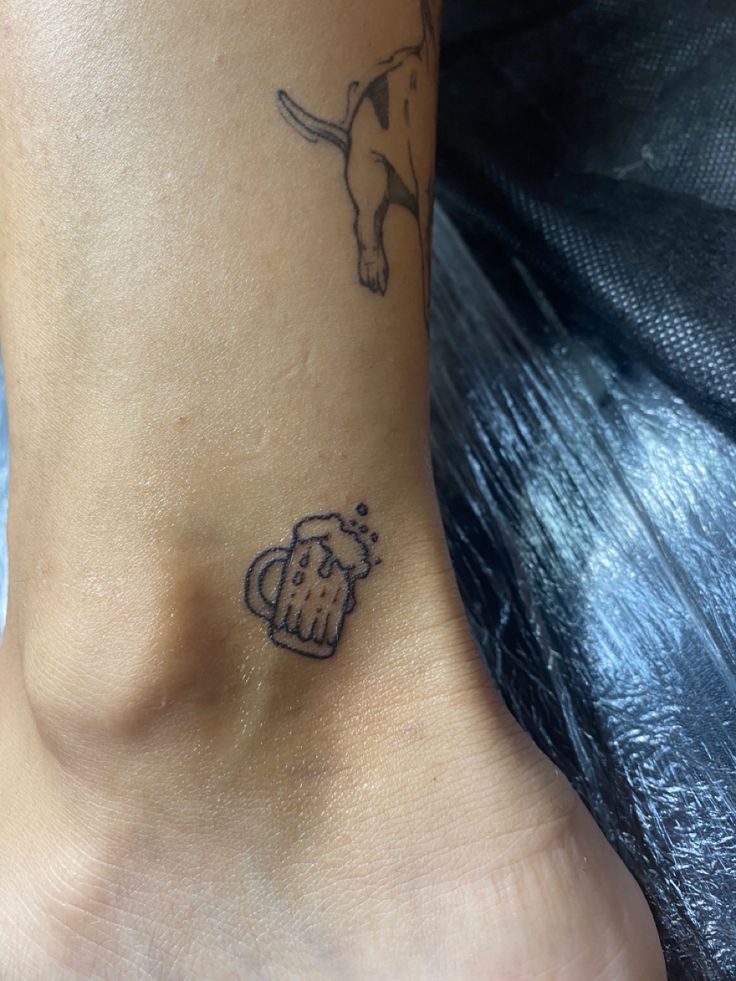 a small tattoo on the ankle of a woman's foot with a beer mug