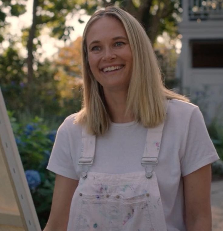 a woman standing in front of an easel smiling at the camera with her hands on her hips