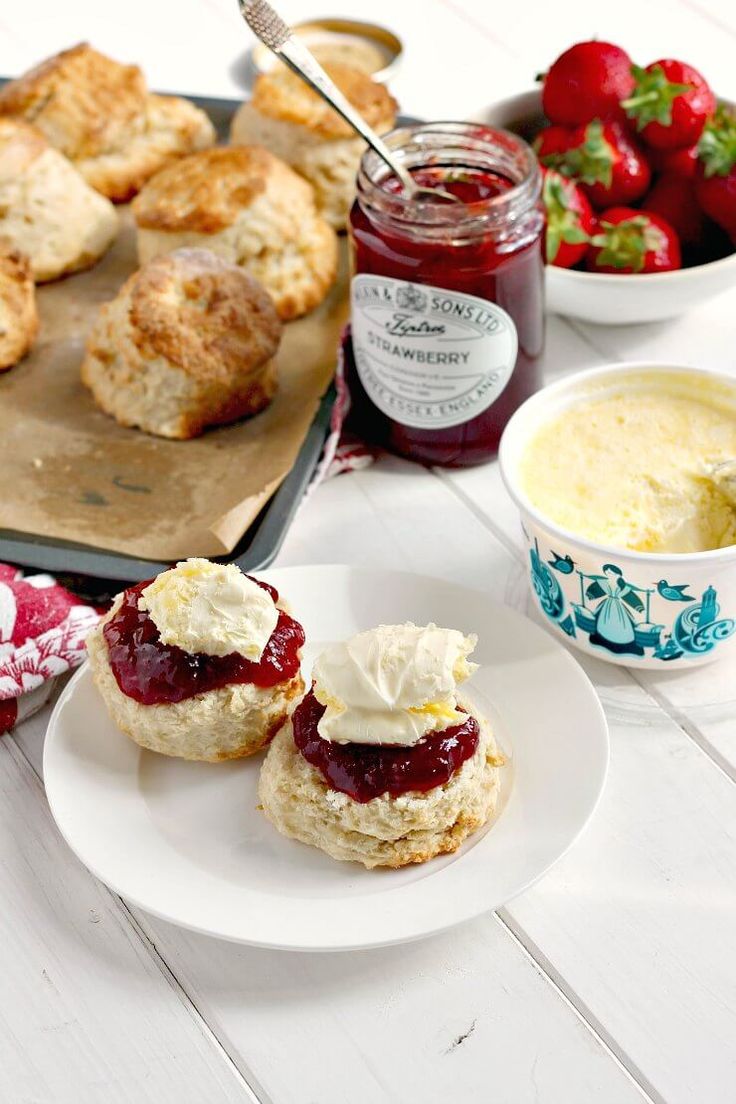 scones with jam, butter and strawberries on a plate next to other food