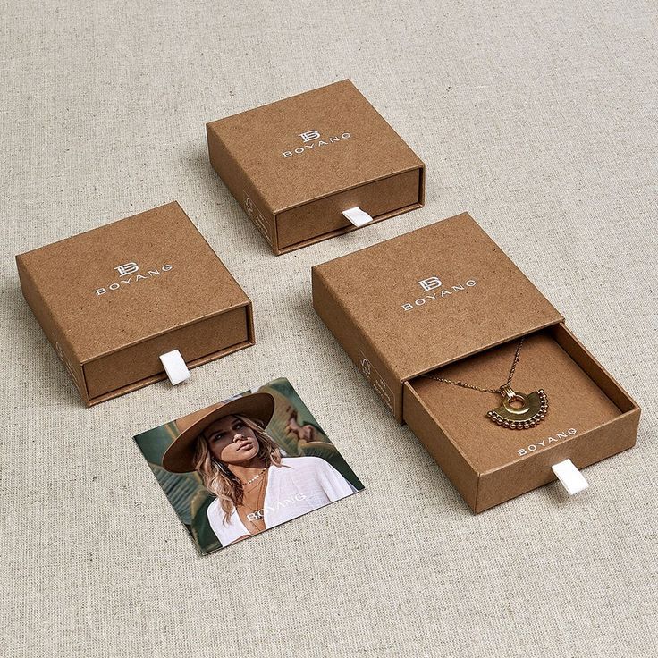 three boxes with necklaces in them sitting on the floor next to a photo and an earring