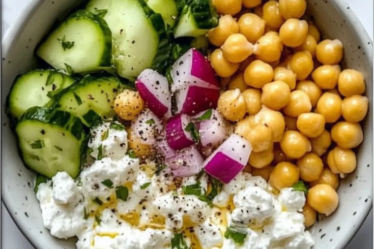 a white bowl filled with cucumbers, chickpeas and other food items