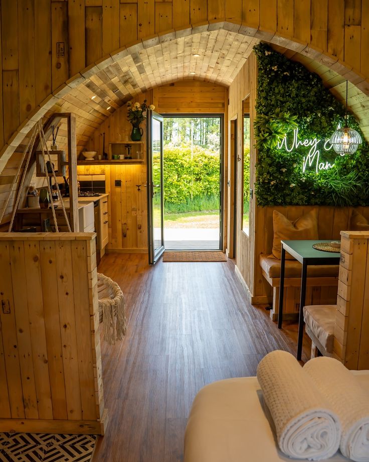 a bedroom with wooden walls and flooring has an arched doorway leading to the outside