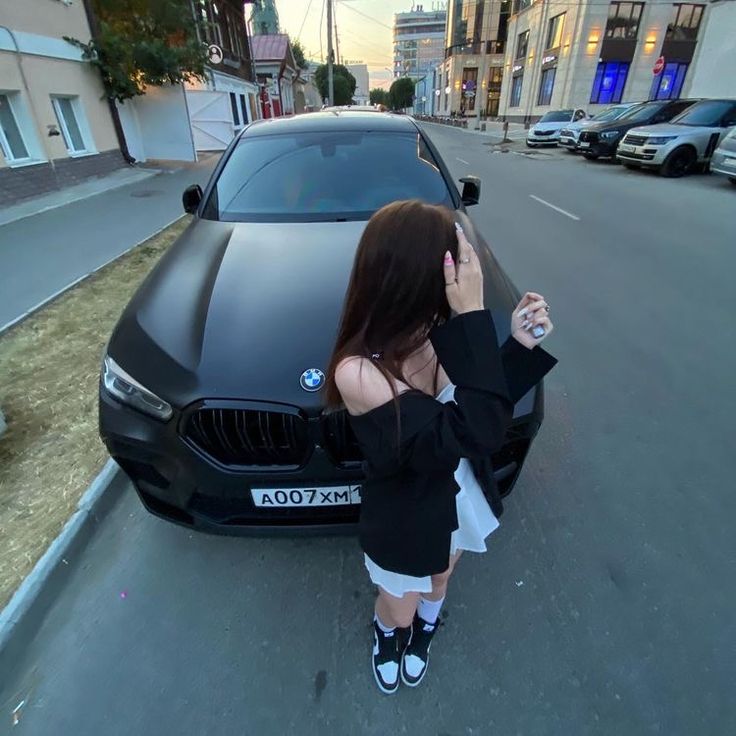 a woman standing in front of a black car