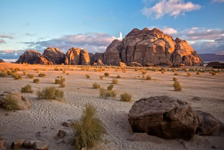 the desert is full of large rocks and small bushes in front of some big rock formations