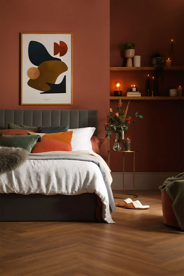 a bed in a bedroom with red walls and orange pillows on the headboard, next to a plant