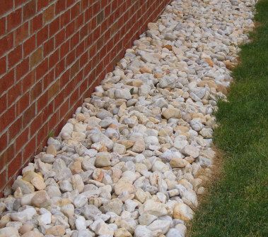 a brick wall next to a lawn with rocks and grass on the ground in front of it