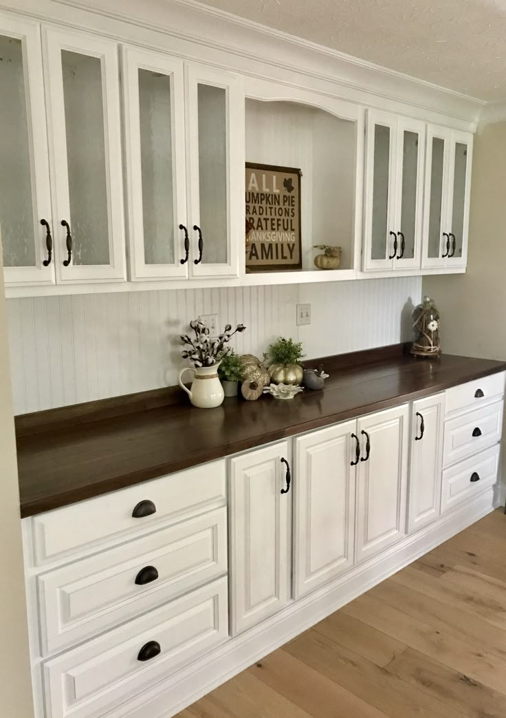 a kitchen with white cabinets and brown counter tops in the middle of wood flooring